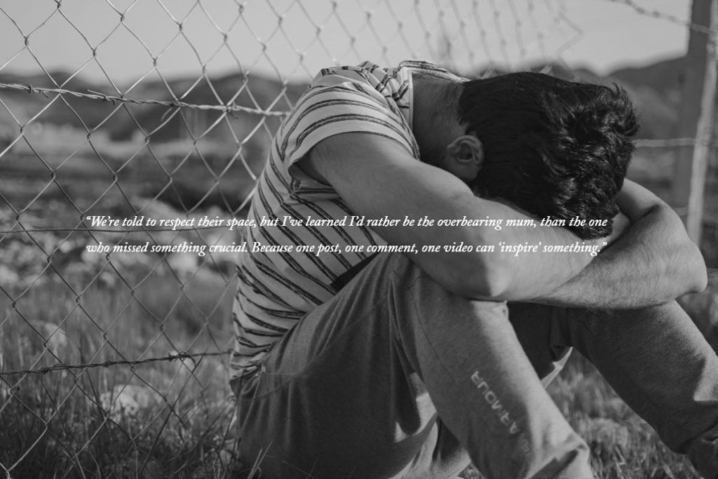 A lad with his head on his knees by a fence