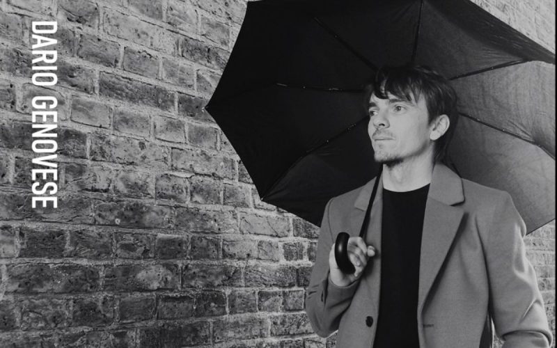 Dario with an umbrella against a brick wall