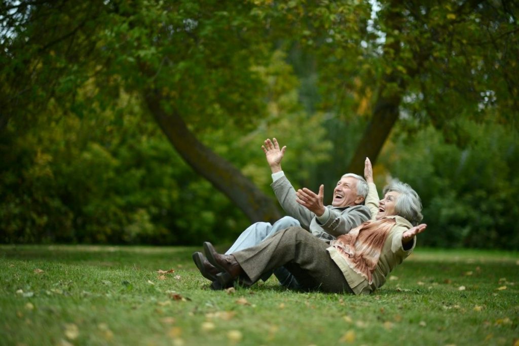 Two elderly people sitting on the grass laughing