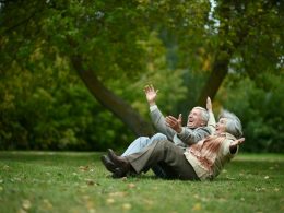 Two elderly people sitting on the grass laughing