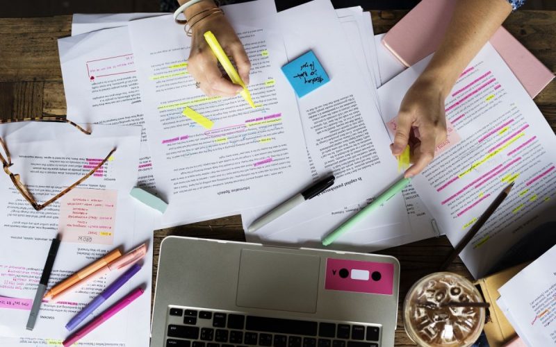 A desk and papers with lots of pens and highlighted information