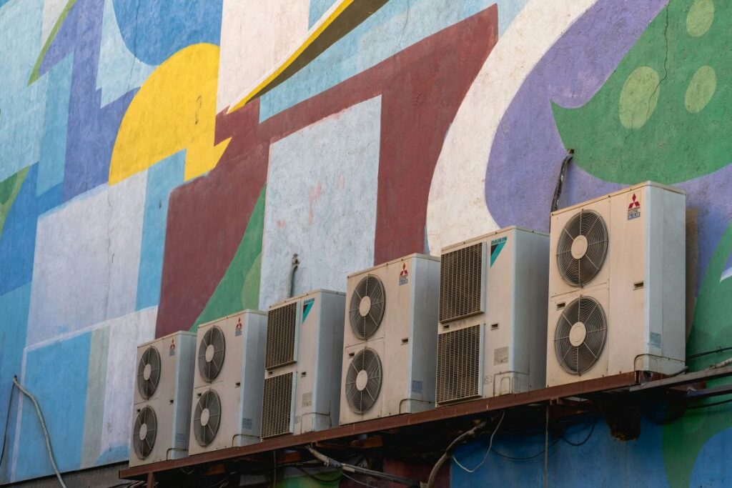 Four outdoor air conditioning units on a brightly-coloured wall