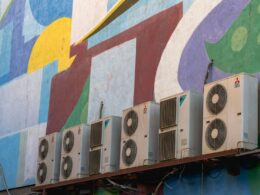 Four outdoor air conditioning units on a brightly-coloured wall
