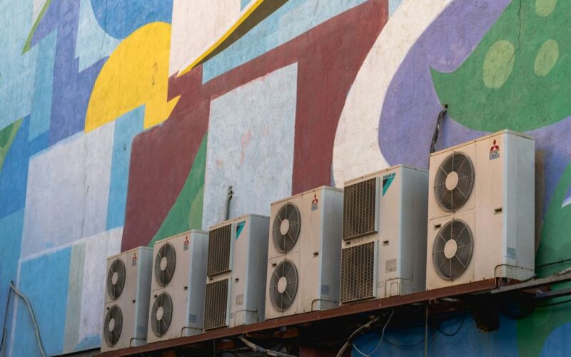 Four outdoor air conditioning units on a brightly-coloured wall