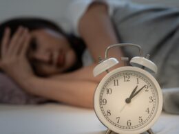 A woman lying awake in bed and her alarm clock