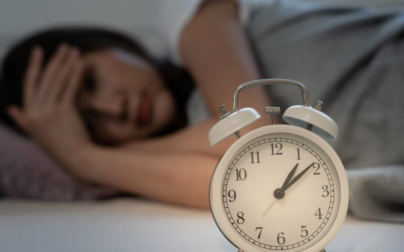 A woman lying awake in bed and her alarm clock