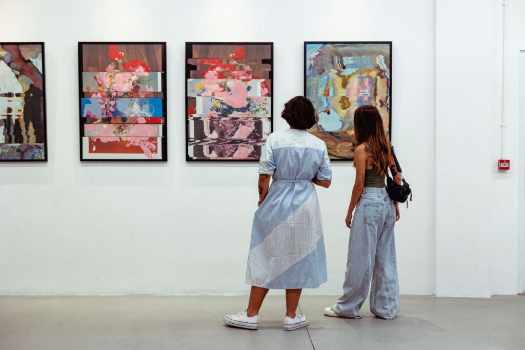 two women look at paintings on a crisp white wall