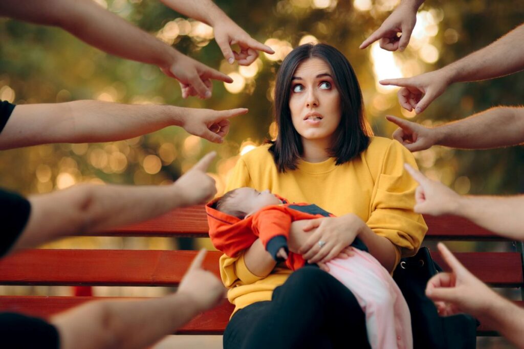 Many hands pointing at a woman with a baby