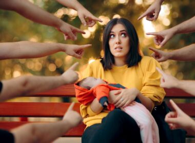 Many hands pointing at a woman with a baby