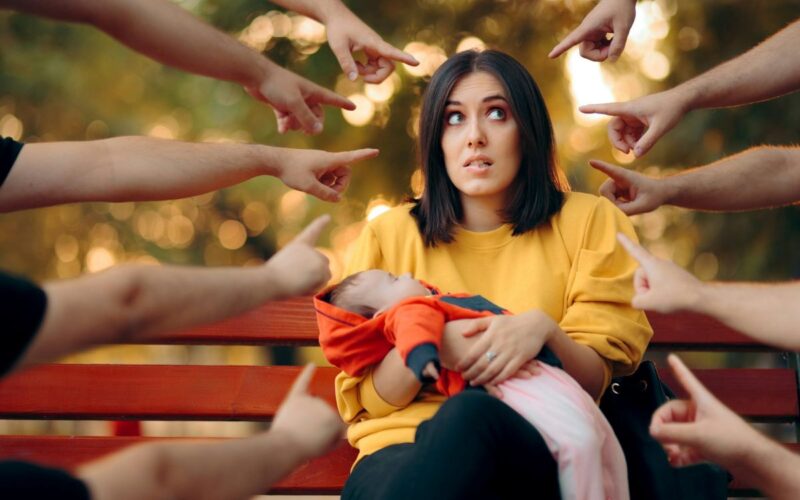 Many hands pointing at a woman with a baby
