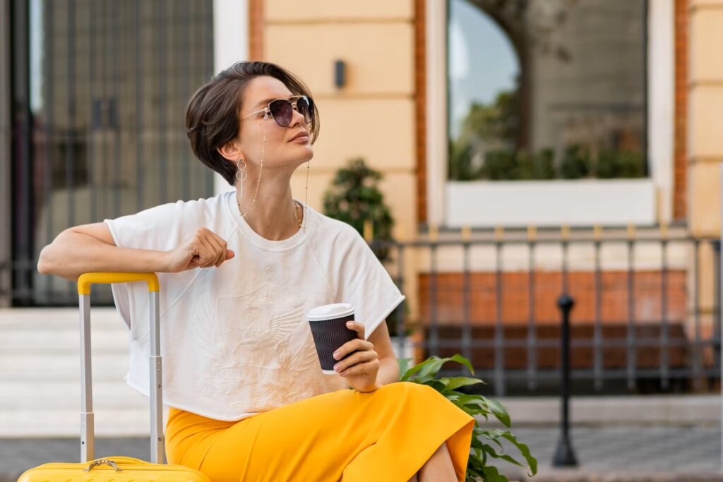 A lady sits on her suitcase waiting and smiling