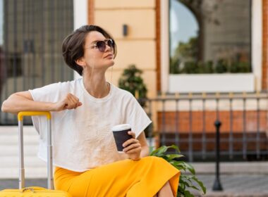 A lady sits on her suitcase waiting and smiling