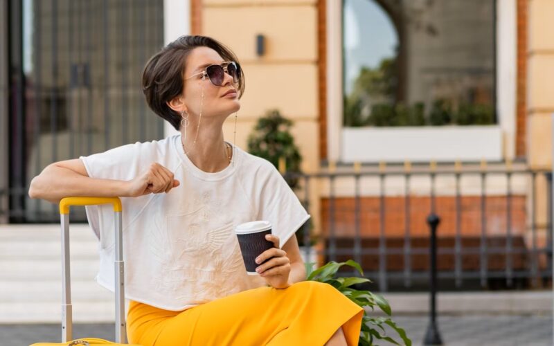 A lady sits on her suitcase waiting and smiling